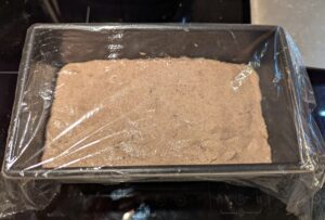 The pan of dough is covered with plastic wrap