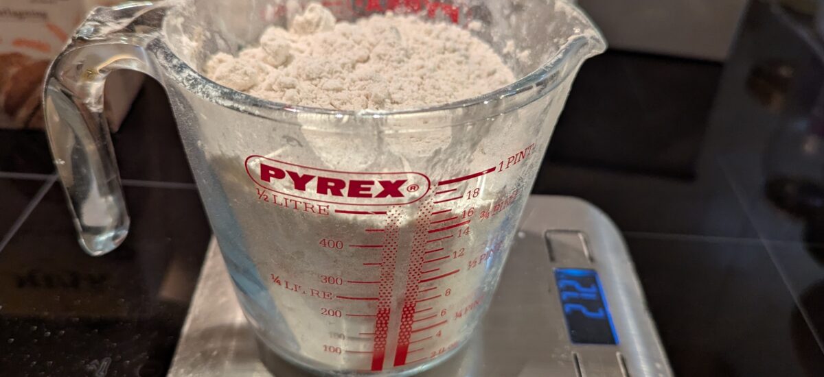 A glass measuring cup of flour blend sits on a digital scale