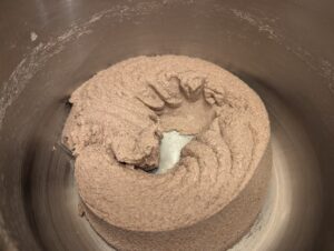 Bread dough in a stand mixer bowl, showing the imprint where the ridged dough roller was pulled out