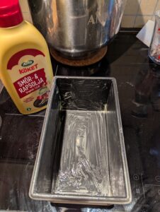 Greased bread pan with a bottle of squeeze margarine next to it