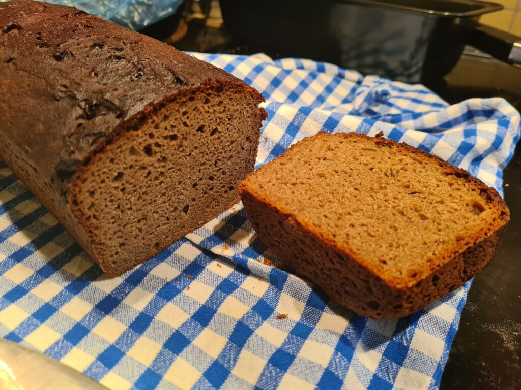 A loaf of dark mock rye bread, with one end sliced off to show the crumb.